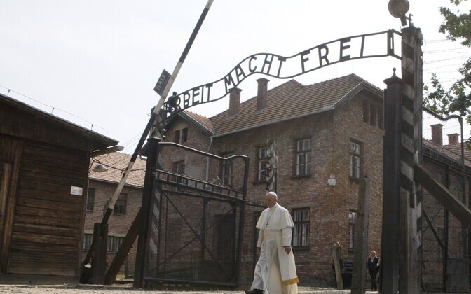 Paavst jalutamas läbi väravate, mille kohal ripub kurikuulus silt 